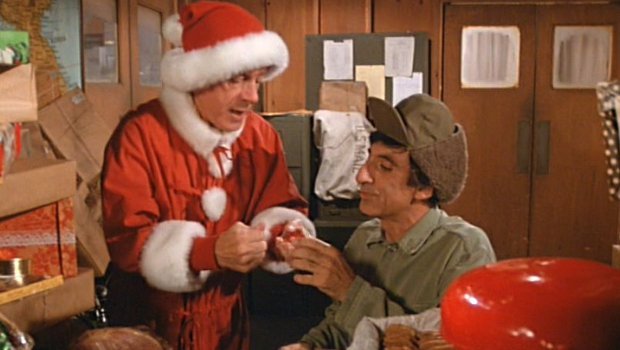 Colonel Potter (Harry Morgan) braucht von Klinger (Jamie Farr) Nähzeug um das Weihnachtskostüm seinem Körperumfang anzupassen.